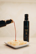 Balsamic vinegar being poured from a bottle onto a plate of food with another bottle in the background.