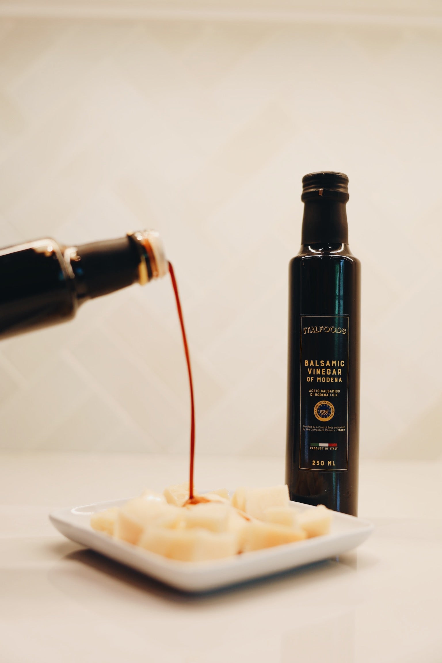 Balsamic vinegar being poured from a bottle onto a plate of food with another bottle in the background.