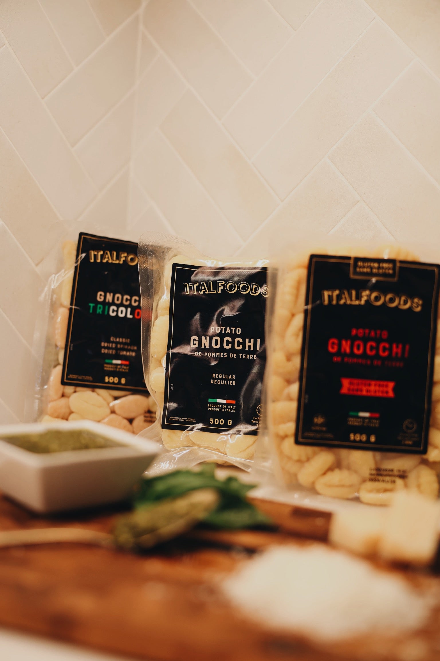 Three packages of ITALFOODS Gnocchi on a wooden surface with a white tiled wall background.